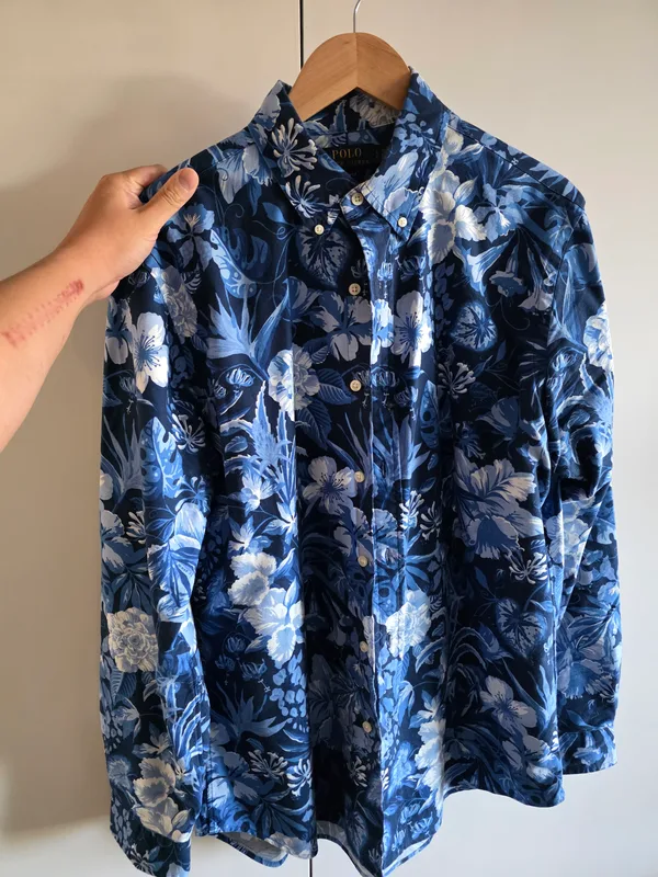 A navy shirt with a blue and white floral print, held up on a hanger against a wall.